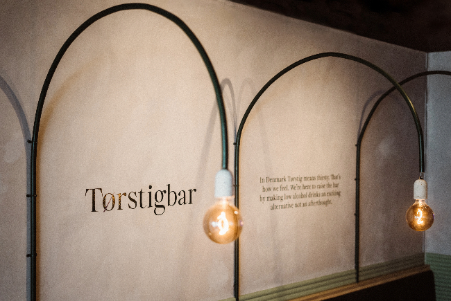 Image showing back wall of Torstigbar, with a quote about the bar and lights in front.
